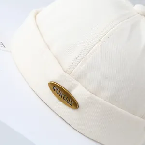 Dettaglio della placca KUKUJI sul cappello Miki in twill di cotone bianco crema