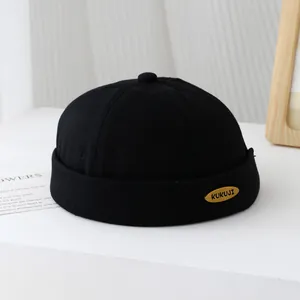 Dettaglio del berretto docker nero con placca in metallo dorato KUKUJI e bordo risvoltato