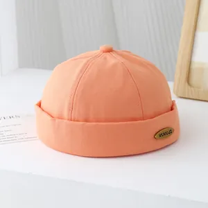 Dettaglio del berretto Miki in cotone arancione con logo KUKUJI metallico su sfondo sobrio