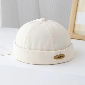 Dettaglio del berretto Miki in cotone beige con trama diagonale e stemma metallico KUKUJI