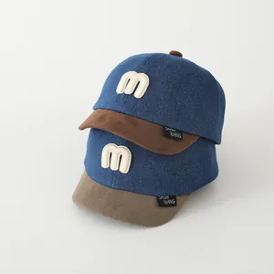 Detail der Kinder-Baseballkappe aus blauem Denim mit braunem Wildlederschirm und M-Stickerei