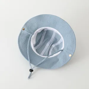Detalle de sombrero de pescador denim con botones dorados y correa ajustable