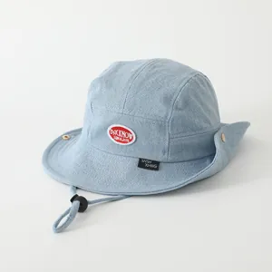 Detail of light blue denim sun hat featuring wide brim, red patch, and adjustable chin strap