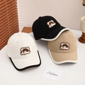 Close-up of baseball caps in black, white and beige with cute brown bear embroidery