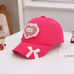 Détail d'une casquette rose pour enfant avec écusson cœur en dentelle et nœud en soie