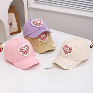 Détail de casquettes enfant avec écussons en cœur et nœuds en ruban en trois couleurs