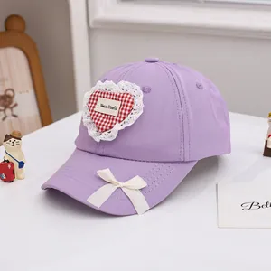 Détail d'une casquette en coton violet avec cœur à carreaux rouges et bordure en dentelle