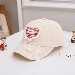 Détail de la casquette en coton crème avec patch cœur en dentelle et petit nœud mignon