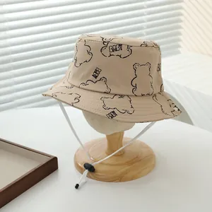 Detalle de gorro de pescador beige para bebé con oso y cordón cortavientos ajustable