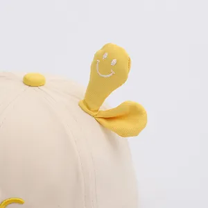Dettaglio cappello beige per neonato con germoglio giallo e faccina sorridente ricamata