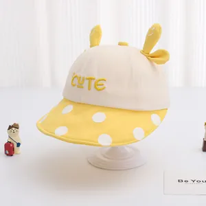 Dettaglio cappello in cotone per bambini con orecchie 3D e tesa gialla a pois su bianco