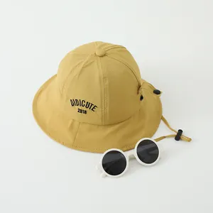 Detalle de gorro de pescador amarillo para niños con bordado, cordón y gafas de sol