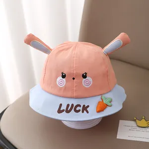 Detail of baby sun hat featuring 3D bunny ears and carrot decor on a beige seat