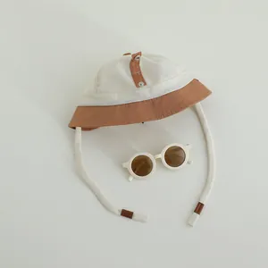 Dettaglio cappello da sole beige in rete con occhiali da sole rotondi coordinati