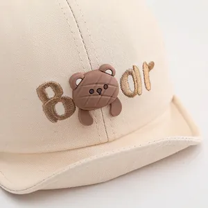Detalle de gorra de bebé en lona beige con bordado de oso de silicona 3D y textura fina