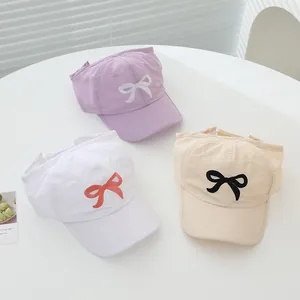 Detailed view of three baseball caps in purple, white, and beige with bow embroidery