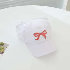 Detail of white cotton baseball cap featuring a red bow embroidery and breathable eyelets
