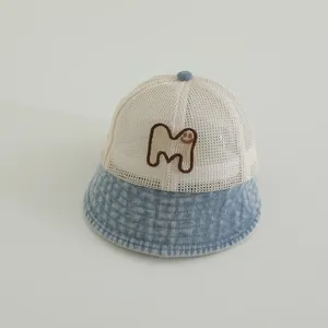 Detail of baby sun hat featuring beige mesh fabric and blue denim brim with M smiley badge