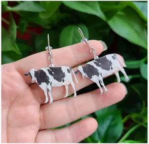 Close-up of cute cow drop earrings with realistic pattern and silver hook earwire