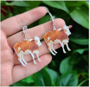 Detail of yellow and white acrylic cow dangle earrings held against natural leaves