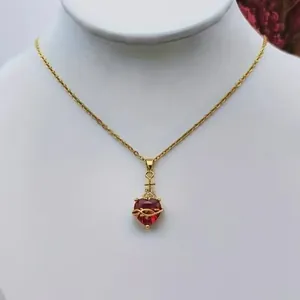 Golden heart necklace with red gem and cross pendant on a white jewelry display