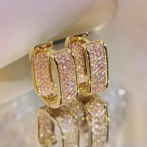 Macro shot of U-shaped gold earrings featuring micro-paved pink zircon stones