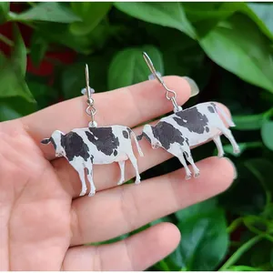 Handheld view of creative acrylic black and white cow earrings with silver hooks