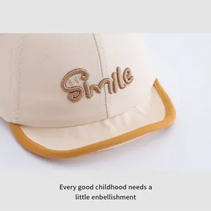 Detailed close-up of brown Smile embroidery on a beige cotton baby sun hat