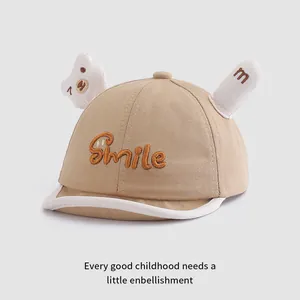 Detail of khaki baby baseball cap with smile embroidery and cute 3D ears on a gray background