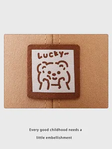 Detalle del parche de osito Lucky cosido en una gorra infantil de lona color caqui