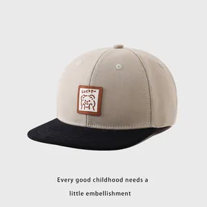 Detalle de gorra de béisbol infantil bicolor con parche de oso Lucky y diseño de visera plana