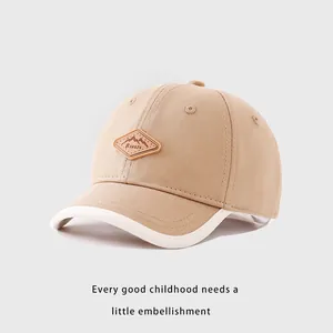 Détail de la casquette bébé avec écusson en cuir et bordure contrastée blanche sur la visière