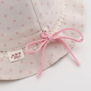 Detail of baby sun hat showing beige polka dot fabric texture and pink bow tie accent