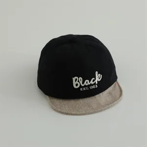 Detail of baby baseball cap with black crown, beige textured brim and white embroidery