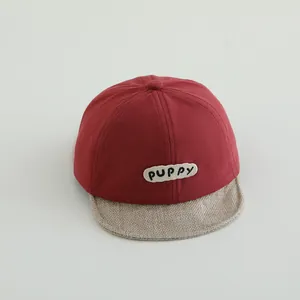 Detail view of red baby baseball cap featuring PUPPY patch and beige textured soft brim