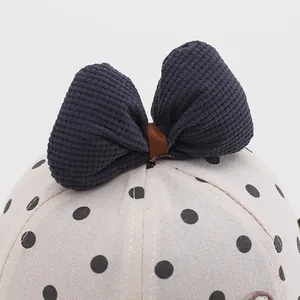 Detail of baby sun hat featuring navy corduroy bow and black polka dots on cotton fabric