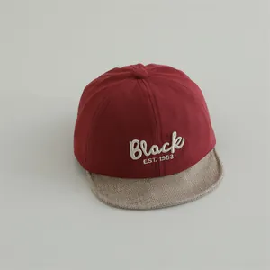 Close-up of baby baseball cap with red fabric and beige woven brim featuring Black embroidery