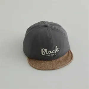 Detailed close-up of grey baseball cap with BLACK embroidery and brown linen brim