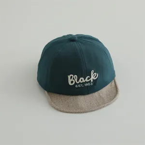 Detail of baby baseball cap featuring Black embroidery and linen texture brim