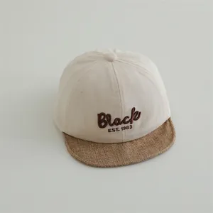 Detail of baby baseball cap featuring Black embroidery and mixed fabric texture