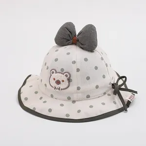 Close-up of beige sun hat featuring green polka dots, bear embroidery and bow details