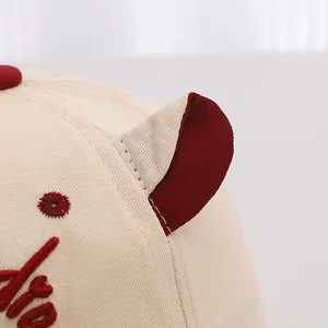 Détail d'une casquette bébé en sergé de coton avec broderie bordeaux et petites oreilles