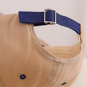 Detail of adjustable metal buckle and blue strap on khaki cotton baseball cap back