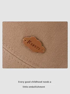 Close-up of the KUKUJI leather cloud patch on a brown twill bucket hat for kids
