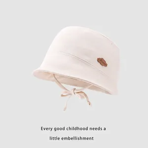 Detail of baby sun hat featuring soft cream cotton fabric and brown cloud patch detail