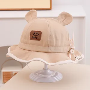 Détail d'un chapeau bob pour bébé kaki avec oreilles d'ours, écusson sourire et jugulaire