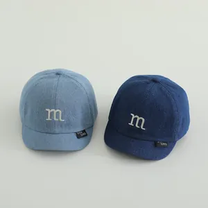 Macro detail of kids denim baseball caps showing M embroidery and fabric texture