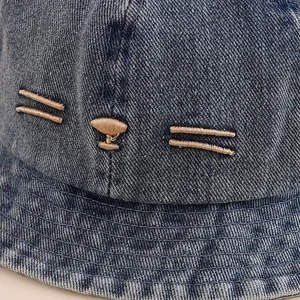 Detail of blue denim baby sun hat featuring gold kitten face embroidery and fine stitching