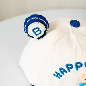 Detail of baby baseball cap featuring blue Happy embroidery and cute bear ornament