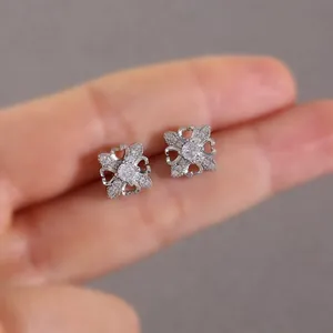 Elegant silver four-leaf clover stud earrings with sparkling cubic zirconia held by hand